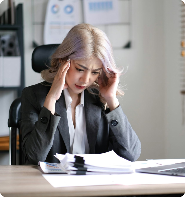 Business Owner with hands on her face looking stressed and isolated, staring at a pile of papers and could potentially benefit from a management consultant's help.